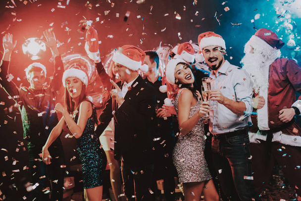 Happy Young People Dancing on New Year Party. Santa Claus. People in Red Caps. Happy New Year Concept. Glass of Champagne. Celebrating of New Year. Young Woman in Dress. Men in Suits. - Photo, image
