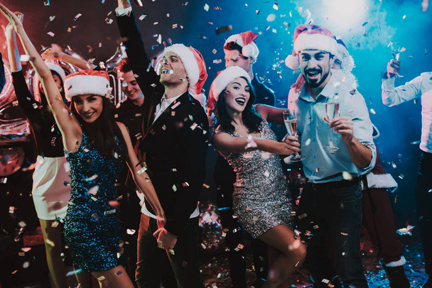 Happy Young People Dancing on New Year Party. Santa Claus. People in Red Caps. Happy New Year Concept. Glass of Champagne. Celebrating of New Year. Young Woman in Dress. Men in Suits. - 写真・画像