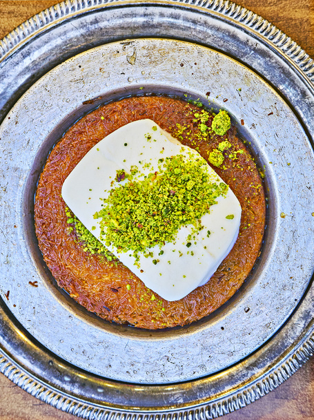 Кунефе, также известный как Кенафе, традиционный арабский десерт, приготовленный из тонкой кондитерской лапши Кадаиф, пропитанный сладким сиропом, слоистый мороженым и увенчанный измельченными фисташковыми орехами
. - Фото, изображение