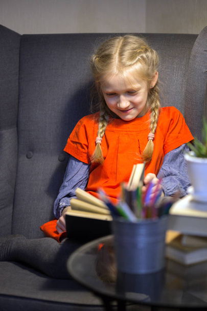 little girl is sitting in a chair and is reading a boo - Foto, afbeelding