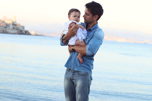 ビーチで彼の女の赤ちゃんを保持しているハンサムな若い父親  - 写真・画像
