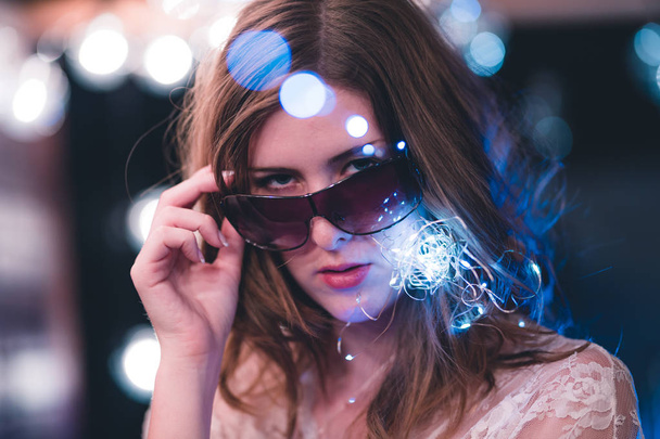 Attractive young caucasian woman poses with string lights with heavy bokeh - Фото, изображение