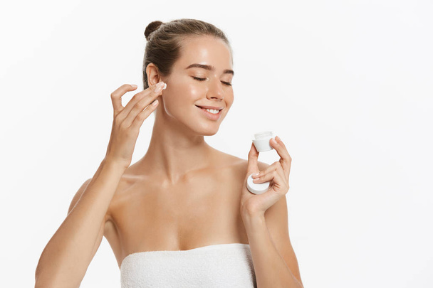 Hermosa mujer joven aplicando tratamiento de crema cosmética en su cara aislada sobre fondo blanco
 - Foto, imagen