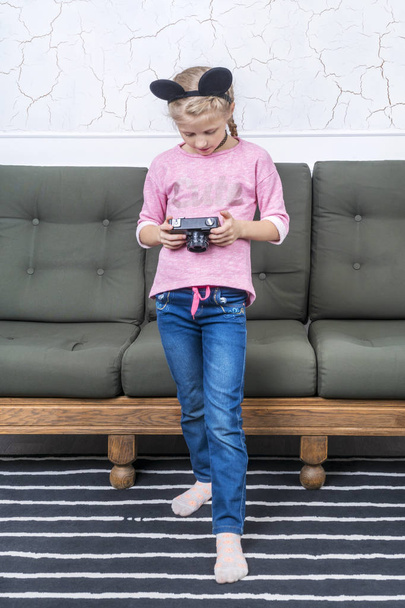 young girl in a mouse costume is standing by the sofa and looking at her camera, looking at photos - Foto, imagen