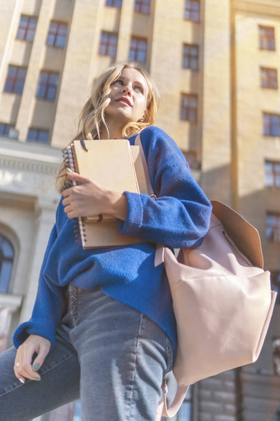 Nice student with notebooks pressed to her chest at the university building in sunny weather - Fotoğraf, Görsel