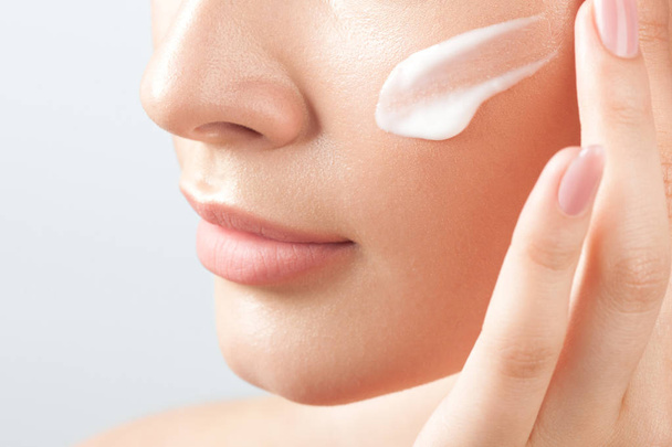 Young beautiful woman applies cream on clean perfect skin.  Beauty portrait close-up - Φωτογραφία, εικόνα