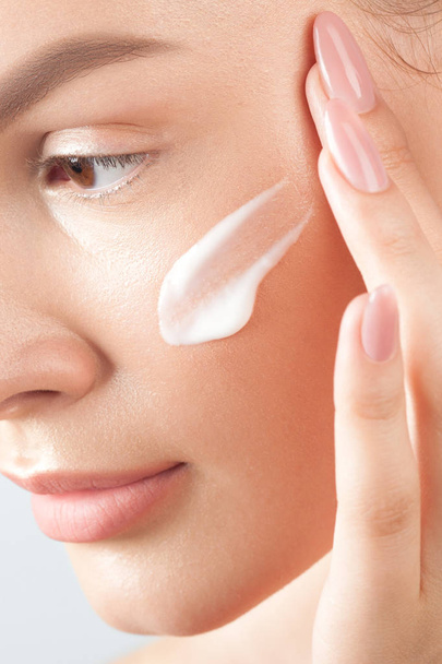 Young beautiful woman applies cream on clean perfect skin.  Beauty portrait close-up - Fotografie, Obrázek