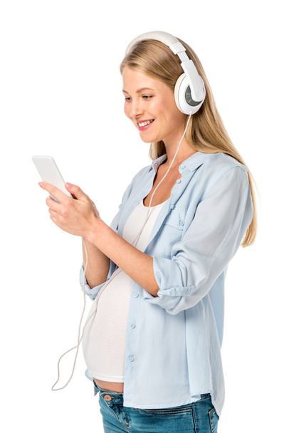 feliz mujer embarazada escuchando música con auriculares y teléfono inteligente aislado en blanco
 - Foto, Imagen