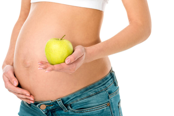 cropped view of pregnant woman touching belly and holding green apple isolated on white - Foto, afbeelding