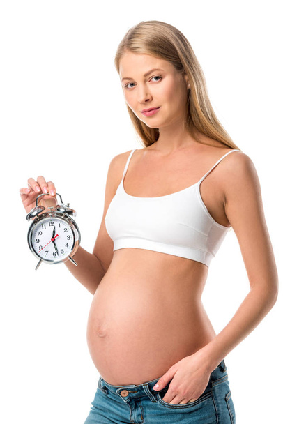 mooie zwangere vrouw houden wekker geïsoleerd op wit - Foto, afbeelding