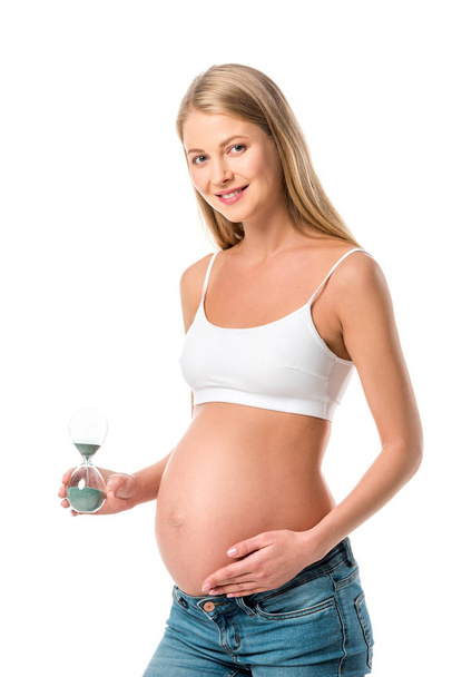 atractiva mujer embarazada sosteniendo reloj de arena aislado en blanco
 - Foto, imagen