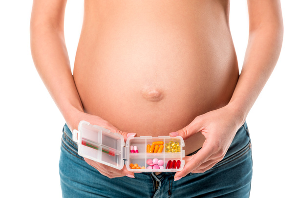 cropped view of pregnant woman holding pill box with vitamins near her belly isolated on white - Foto, Imagen
