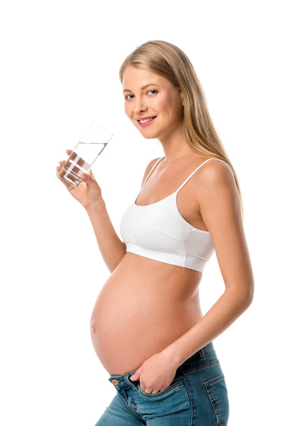 smiling pregnant woman in white bra holding glass of pure water isolated on white - Photo, Image