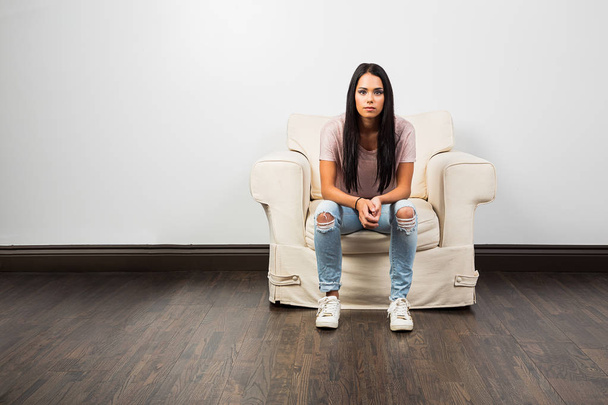 mid-twenties young woman wearing jean with hold on the knees, sitting on a couch - 写真・画像