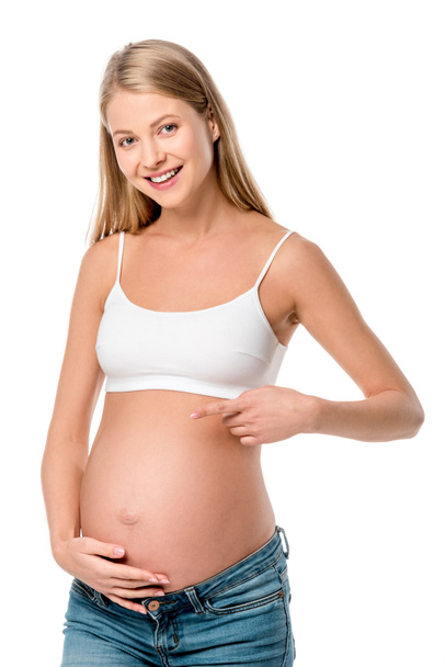 白で隔離彼女のおなかを指して白ブラで妊娠中の女性の笑顔 - 写真・画像