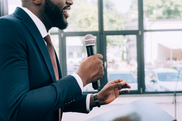 abgeschnittenes Bild eines lächelnden afrikanisch-amerikanischen Sprechers, der während eines Seminars im Konferenzsaal ins Mikrofon spricht - Foto, Bild