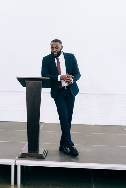 pěkný africký americký podnikatel opírající se o pódium tribun a mluvení během semináře v konferenčním sále - Fotografie, Obrázek