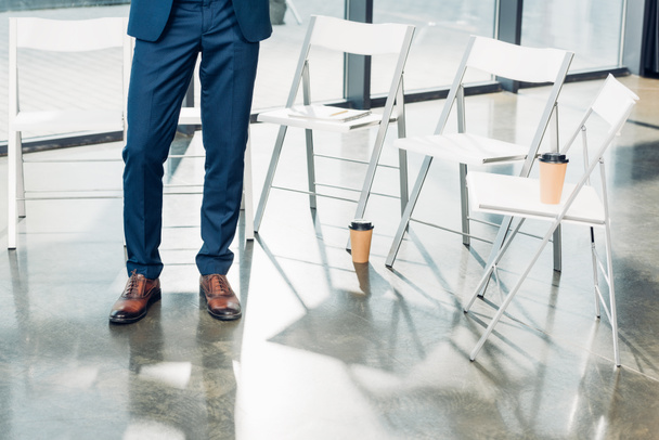 частковий вид на бізнесмена, що стоїть біля порожніх стільців у конференц-залі
 - Фото, зображення