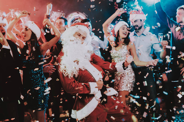 Man in Santa Claus Costume on New Year Party. Happy New Year. People Have Fun. Indoor Party. Celebrating of New Year. Young Women in Dresses. Young Men in Suits. Happy People. Man with White Beard. - Φωτογραφία, εικόνα