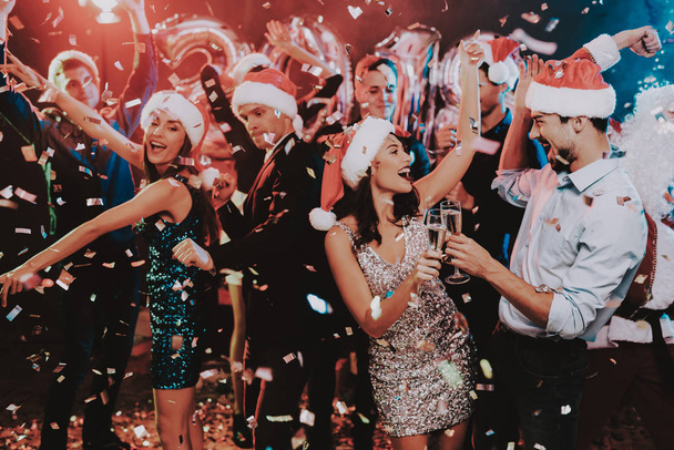 Happy Young People Dancing on New Year Party. Santa Claus. People in Red Caps. Happy New Year Concept. Glass of Champagne. Celebrating of New Year. Young Woman in Dress. Men in Suits. - Фото, изображение