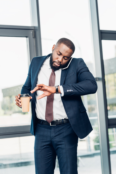 homme d'affaires afro-américain avec café pour aller vérifier l'heure tout en ayant une conversation sur smartphone dans la salle de conférence
 - Photo, image