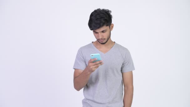 Young happy bearded Indian man using phone and looking surprised - Video