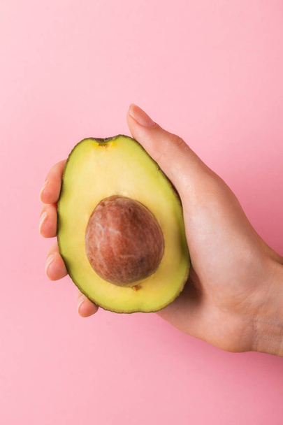 Half of avocado with kernel in female hand on bright pink background. Horizontal view. Copy space - 写真・画像
