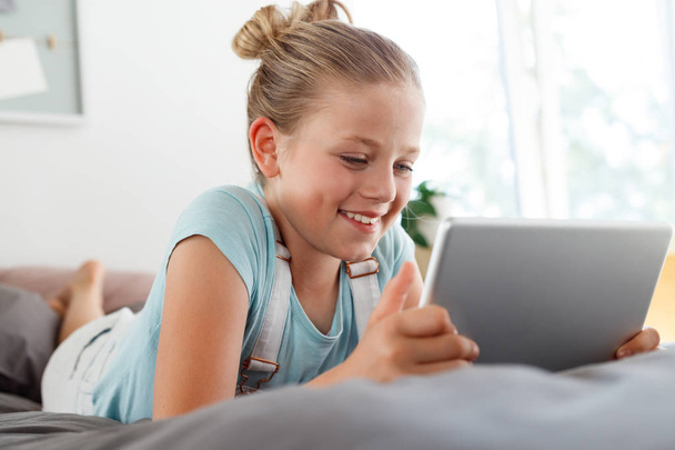 Smiling girl lying down on bed in her room and using a digital tablet. Close up of face. - Fotoğraf, Görsel