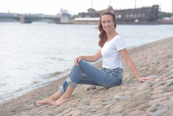 woman in jeans and white t-shirt sits by the water - Foto, imagen