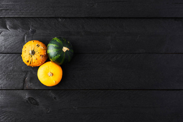 Simple autumn background with yellow, orange and green pumpkins on black wood with copy space. Top view. - Фото, зображення