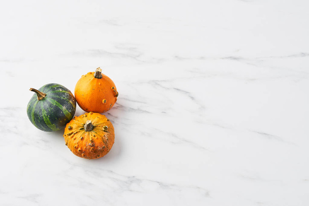 Top view of yellow, green and orange pumpkin on white marble table. Selective focus, copy space. - Zdjęcie, obraz