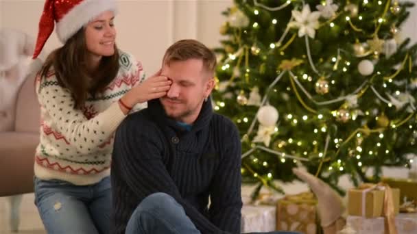 Gyönyörű fiatal pár a szerelem viselt Santa kalap, feküdt a padlón egy kandalló és egy szépen díszített karácsonyfa és élvezi karácsony reggelén. - Felvétel, videó