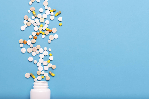 Flacone bianco e pillole multicolori su sfondo blu. Concetto di prodotti farmaceutici, medicina, farmaci e trattamento delle malattie. Posa piatta, vista dall'alto
. - Foto, immagini