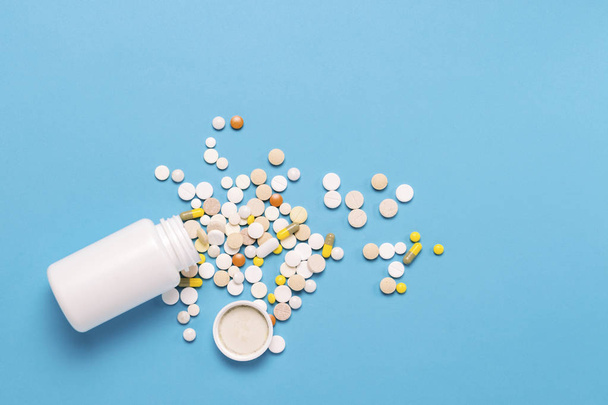 Λευκή φιάλη και πολύχρωμα χάπια σε μπλε φόντο. Έννοια των φαρμακευτικών προϊόντων, ιατρική, φάρμακα και θεραπεία για τις ασθένειες. Επίπεδη lay, κορυφαία προβολή. - Φωτογραφία, εικόνα