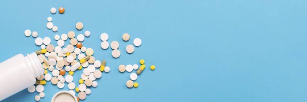 White bottle and multi-colored pills on a blue background. Concept of pharmaceuticals, medicine, drugs and treatment for diseases. Banner. Flat lay, top view. - Photo, Image