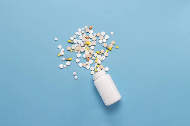 Λευκή φιάλη και πολύχρωμα χάπια σε μπλε φόντο. Έννοια των φαρμακευτικών προϊόντων, ιατρική, φάρμακα και θεραπεία για τις ασθένειες. Επίπεδη lay, κορυφαία προβολή. - Φωτογραφία, εικόνα