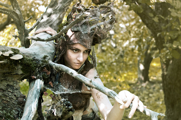 vrouw in een pak van vilt en make-up van natuurlijke remedies en bos puin, de Dryad verbergt in een oude tuin onder de bomen - Foto, afbeelding