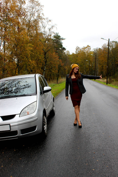 the autumn day the car broke down and the girl in a dress with a hat catches another car to help - Foto, Imagem