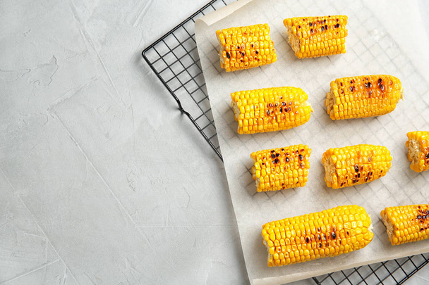 Cooling rack with grilled corn cobs on light background, top view. Space for text - Фото, изображение