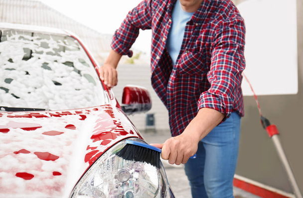 Young man cleaning vehicle with brush at self-service car wash - Фото, зображення