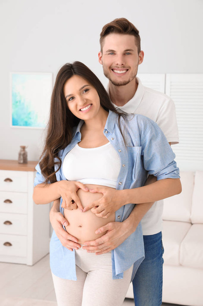 Pregnant woman and her husband showing heart with hands at home - Photo, image