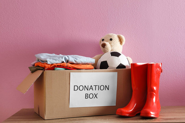 Donation box with clothes and toys on table against color background - Foto, immagini