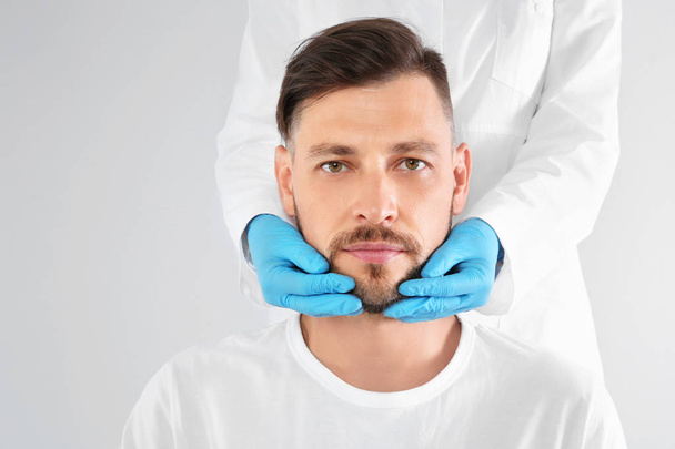 Doctor examining mature man face before cosmetic surgery on white background - Foto, afbeelding