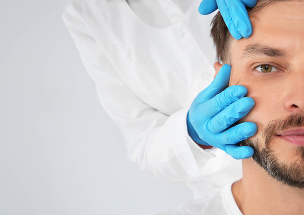Doctor examining mature man face before cosmetic surgery on white background, closeup - Photo, image