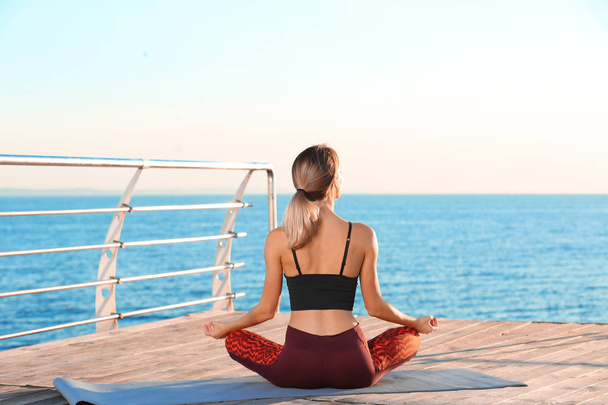 Young woman doing yoga exercises on pier in morning - Photo, image