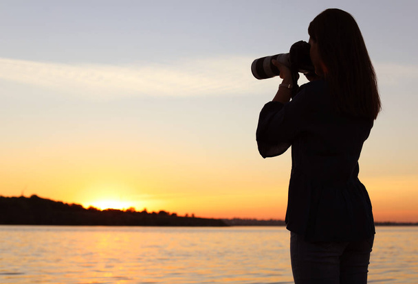 Mladých fotografek pořizování Foto u řeky západu slunce s profesionální kameru venku - Fotografie, Obrázek