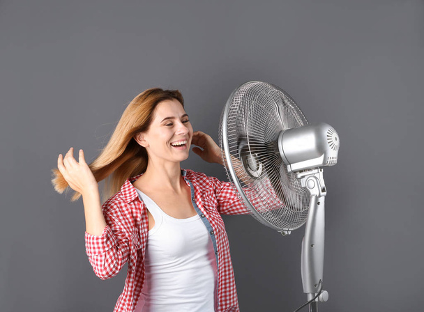 Woman refreshing from heat in front of fan on grey background - Фото, зображення