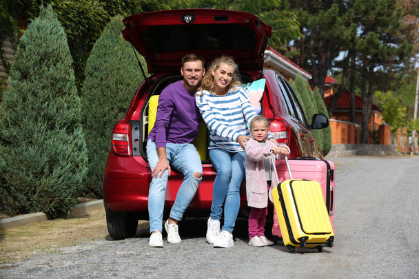 Щаслива молода сім'я біля багажника автомобіля, завантаженого валізами на відкритому повітрі
 - Фото, зображення