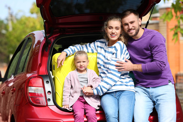 Happy young family near car trunk loaded with suitcases outdoors - Fotó, kép