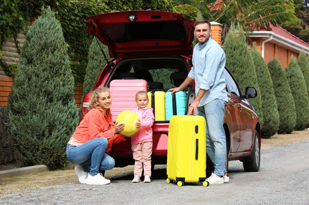 Happy young family near car trunk loaded with suitcases outdoors - Fotó, kép